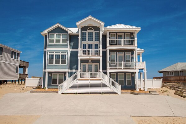 A multi-story beachfront house with a central staircase, balconies, and a sandy beach in the background. - Bellissimo - Oceanfront with Pool, Hot Tub, Theater Room, Elevator, Game Tables (Virginia Beach)