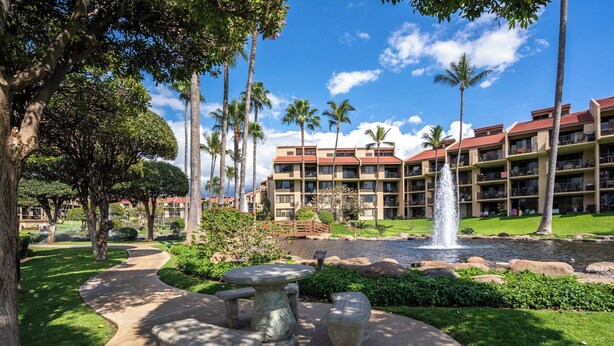 A hotel with a courtyard featuring a fountain, palm trees, and a stone seating area. - Charming Beachside Garden Vistas (Kihei)