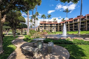 A hotel with a courtyard featuring a fountain, palm trees, and a stone seating area. - Charming Beachside Garden Vistas (Kihei)