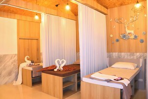 Un cuarto de spa con una camilla de masaje, un armario de madera con botellas y una pared decorada con ciervos y flores.