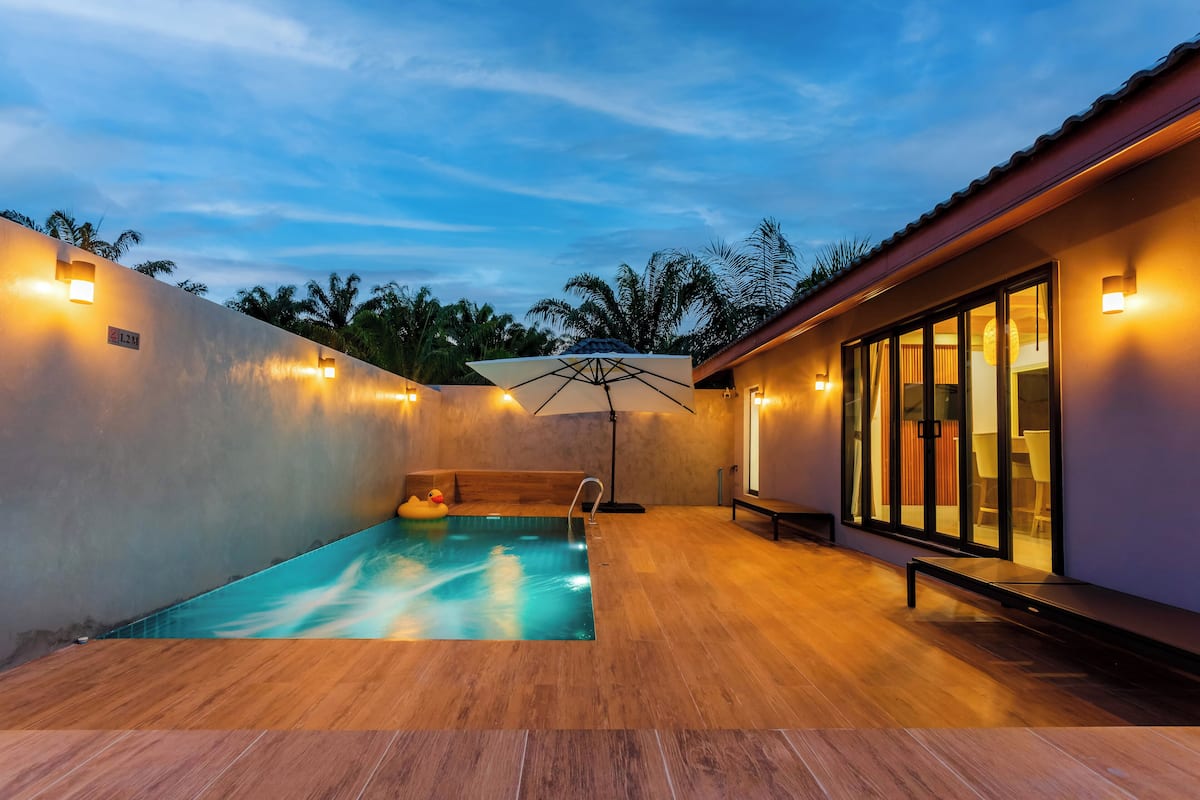 A modern outdoor pool area with a wooden deck, a lounge chair, and a large umbrella.