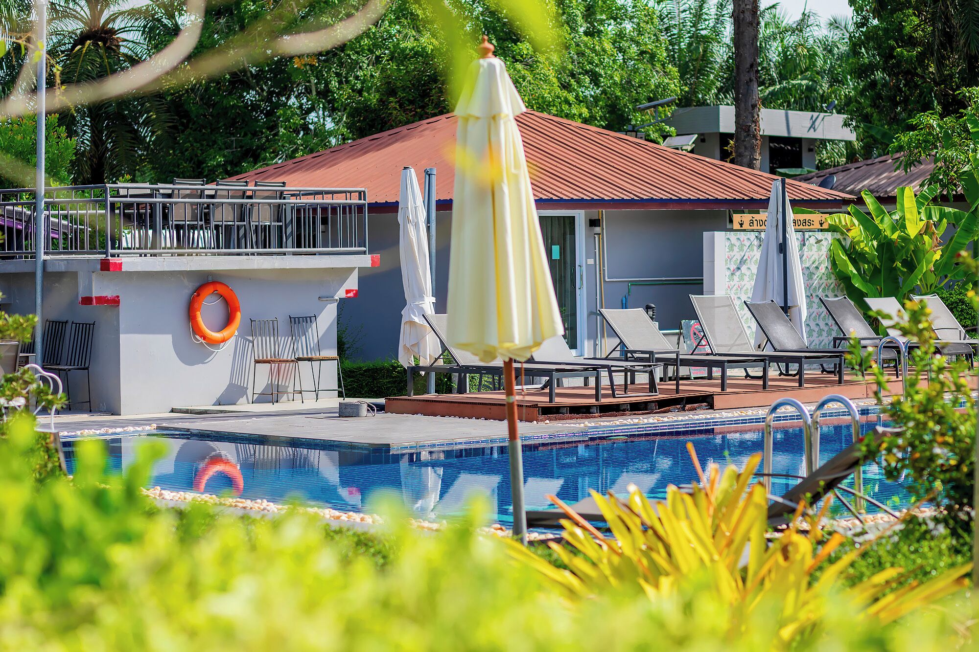 A pool area with lounge chairs, umbrellas, and a lifebuoy.