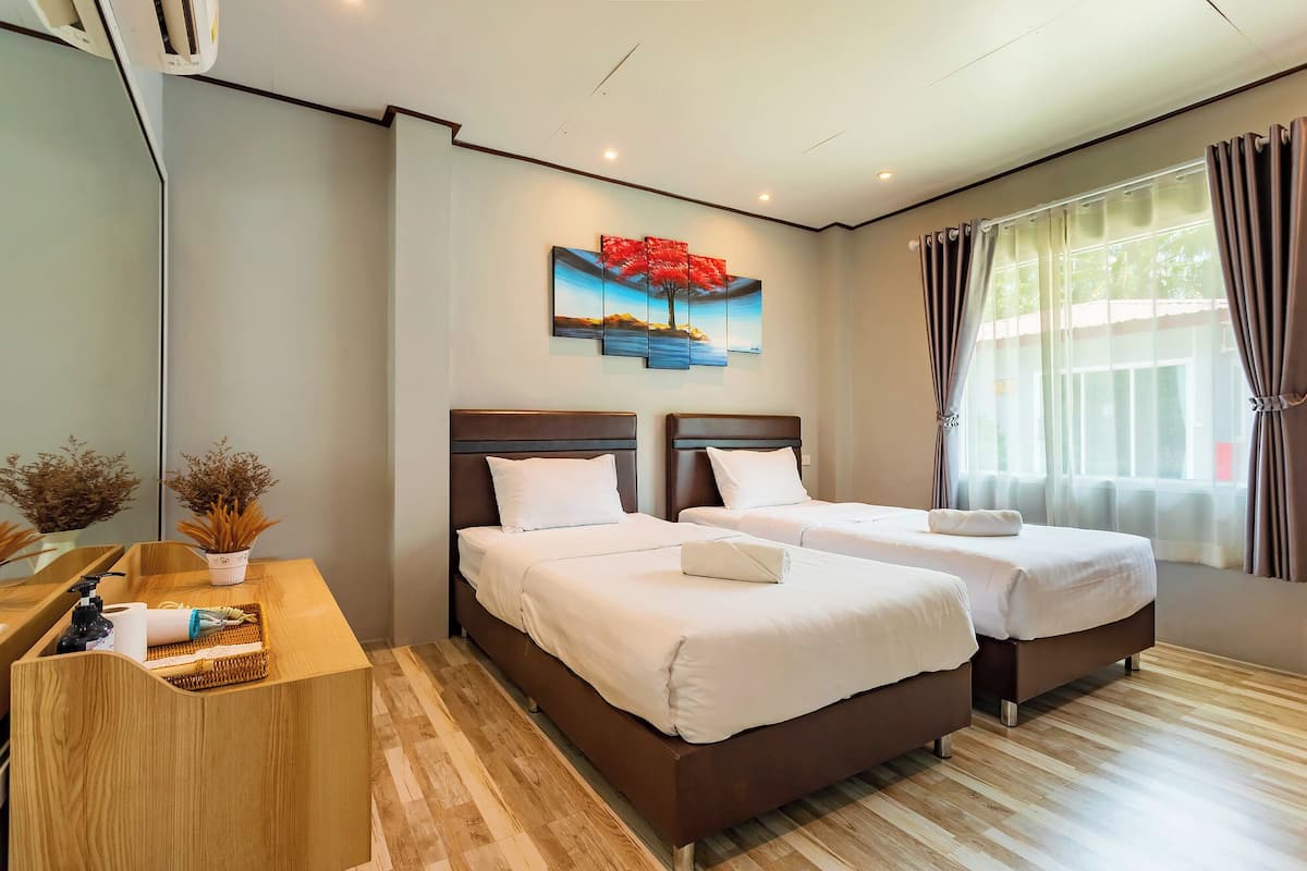 A hotel room with two beds, a wooden desk, a painting on the wall, and a window with curtains.