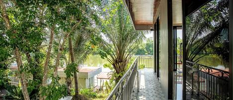 A covered balcony with a view of a river and surrounding greenery.