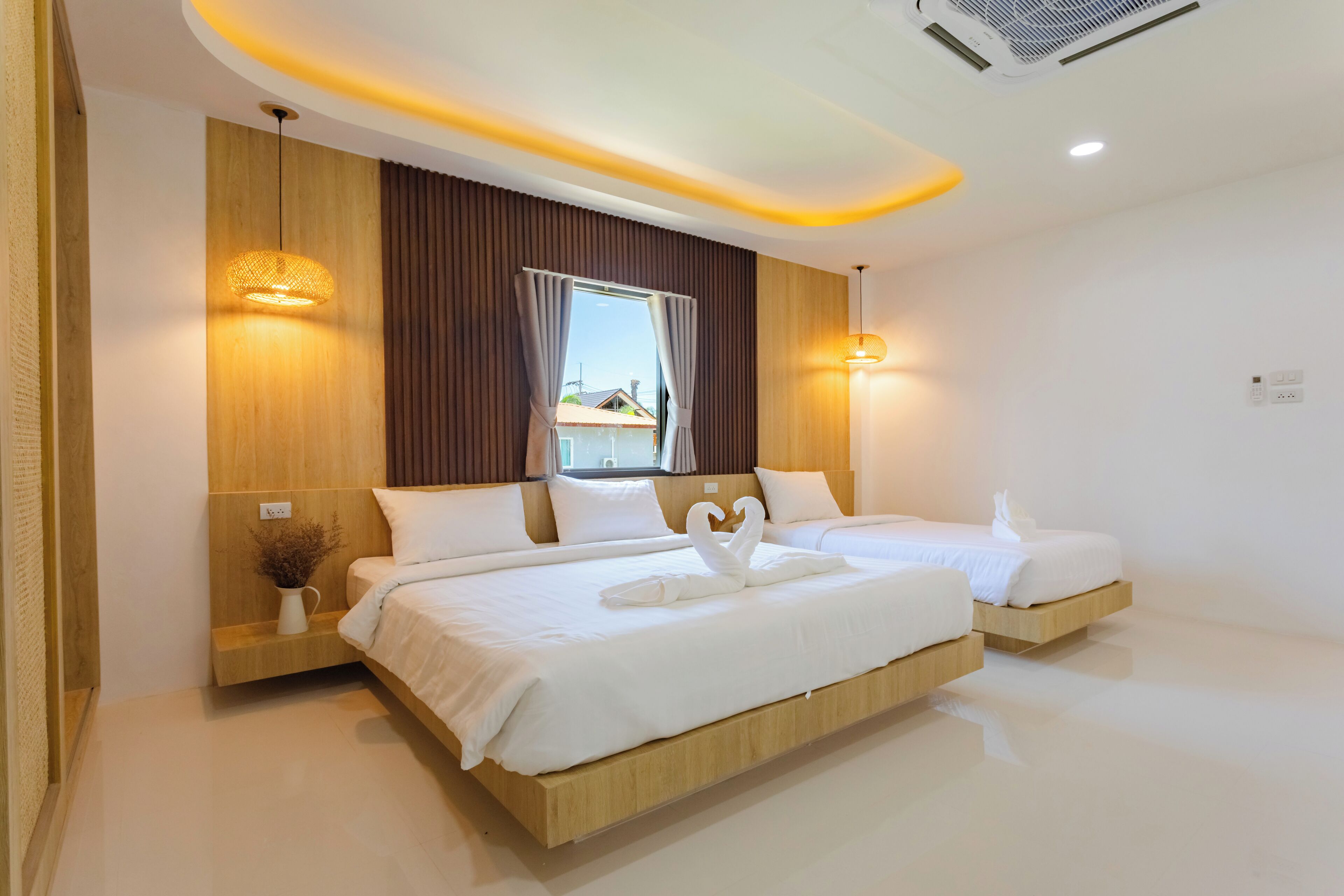 A modern hotel room with two beds, wooden headboards, a large window with curtains, and a vase with dried flowers.