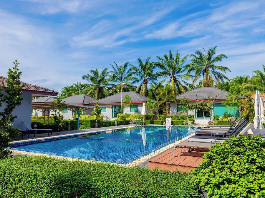 A swimming pool surrounded by lush greenery and palm trees, with a clear blue sky above.