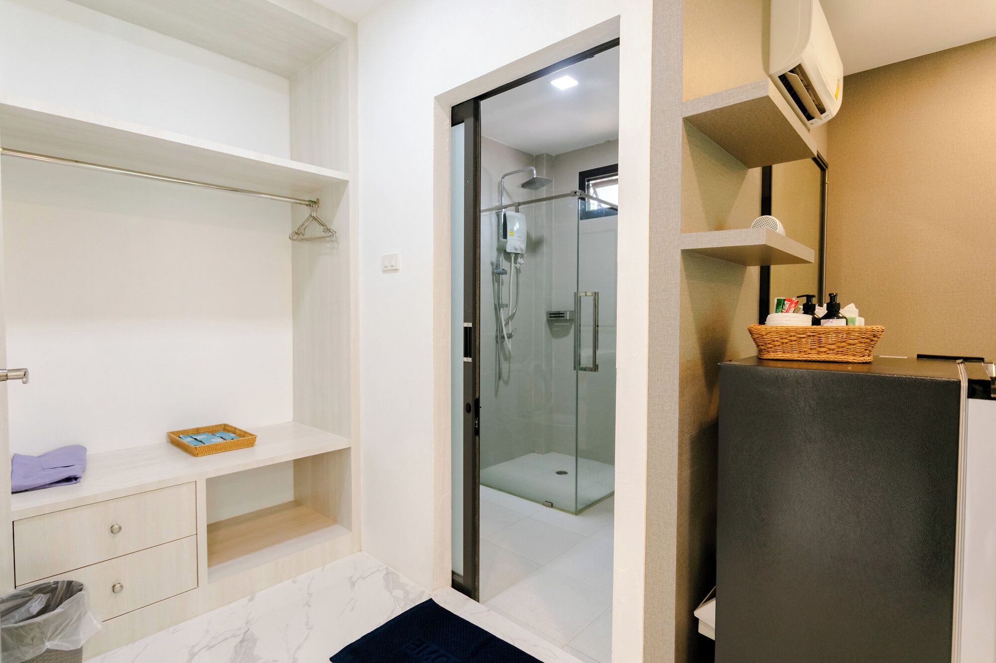 A modern bathroom with a glass shower enclosure, a white vanity with a basket of toiletries, and a marble-tiled floor.