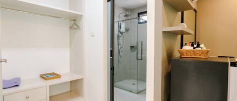 Un baño moderno con cabina de ducha de vidrio, tocador blanco con un cesto de artículos de aseo, y suelo de baldosas de mármol.