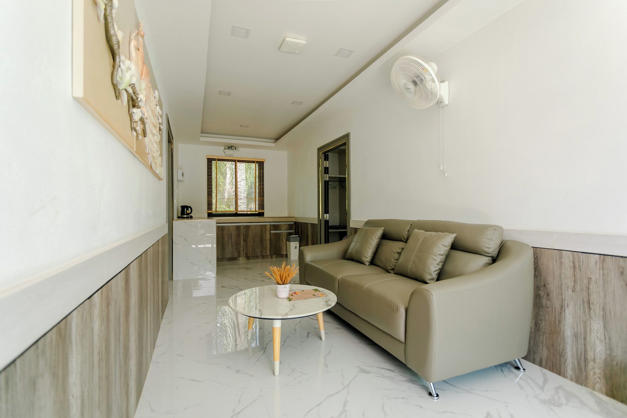 A modern living room with a beige sofa, a glass coffee table, and a white fan.