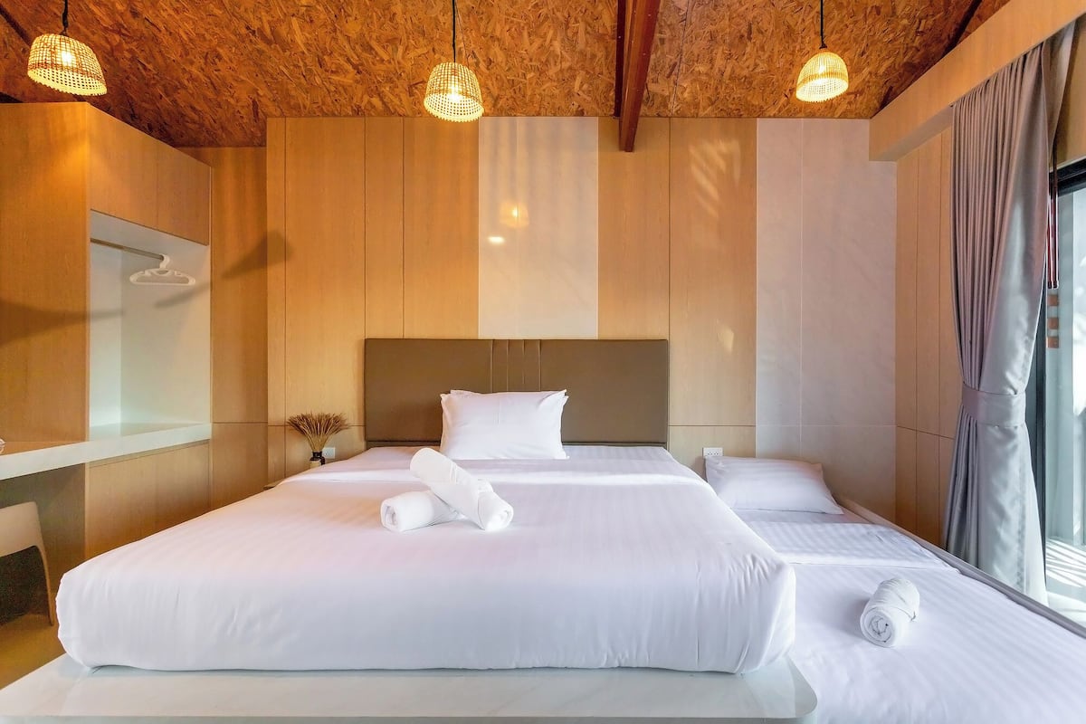 A hotel room with a wooden ceiling, two beds with white linens, a large mirror, and a window with curtains.
