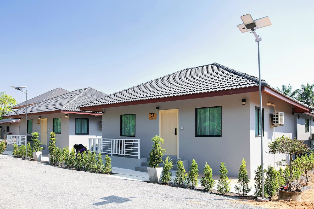A row of modern, single-story buildings with tiled roofs, numbered signs, and small potted plants in front.