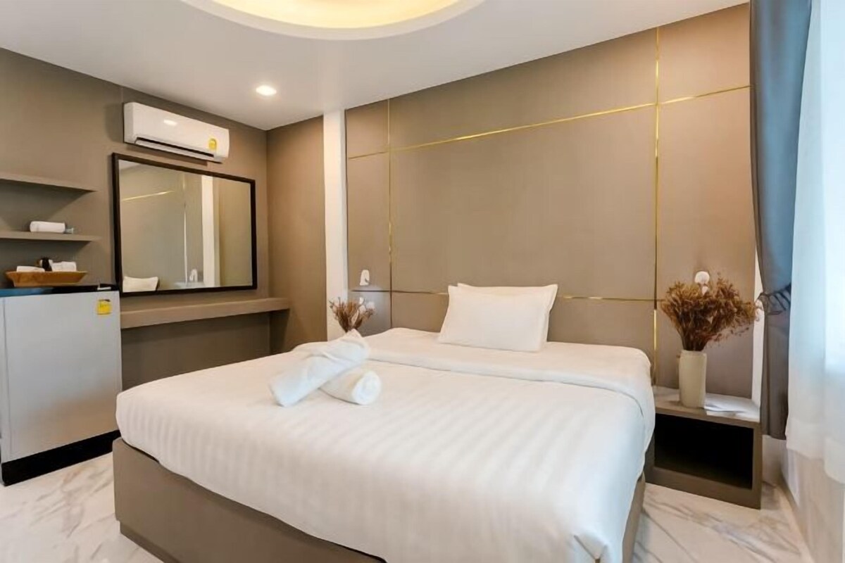 A hotel room with a large bed, a bedside table, a mirror, and a wall-mounted air conditioning unit.