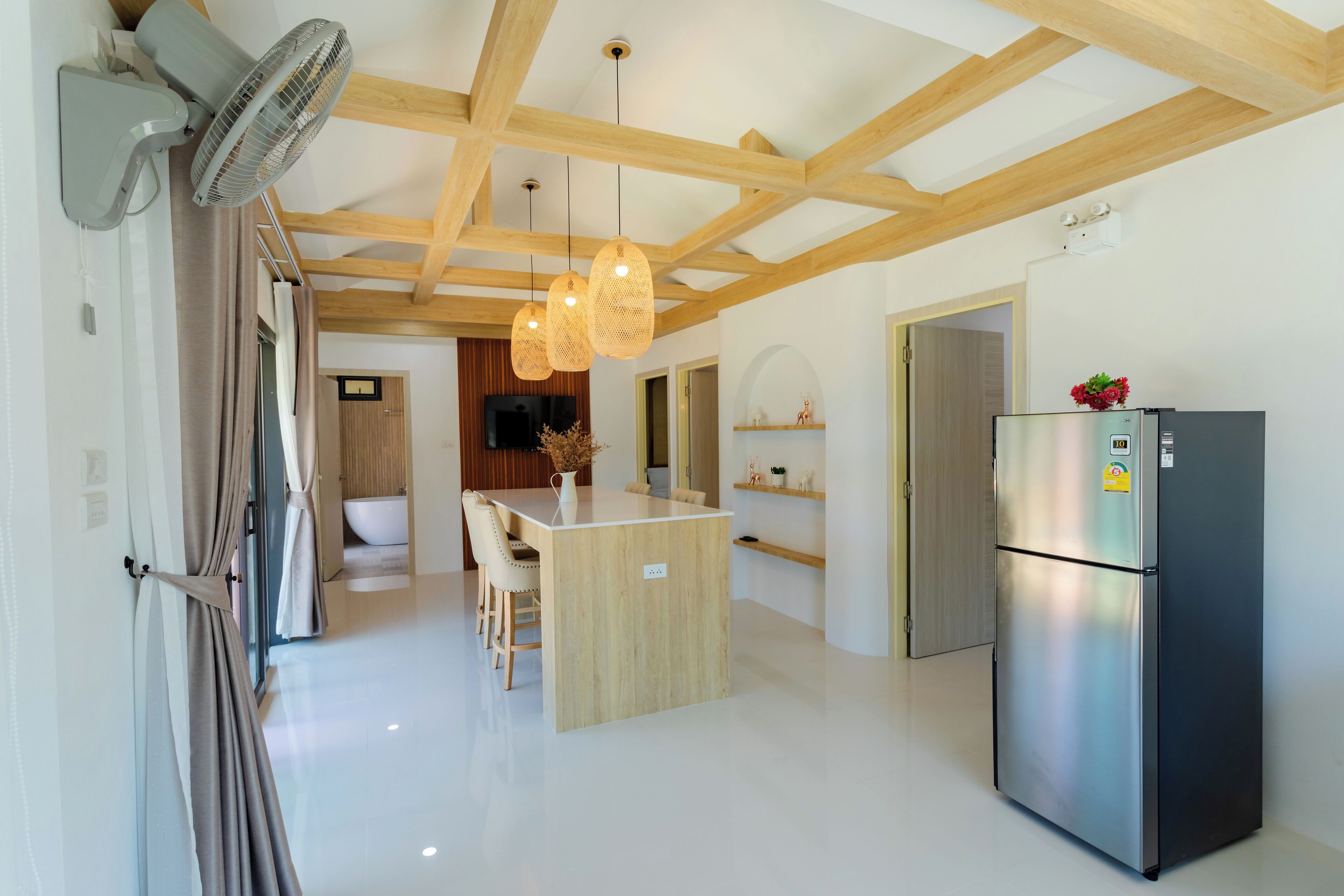 Una cocina moderna con una isla central, vigas de madera en el techo, un refrigerador empotrado y un comedor con sillas.