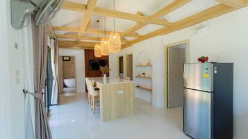 Una cocina moderna con una isla central, vigas de madera en el techo, un refrigerador empotrado y un comedor con sillas.