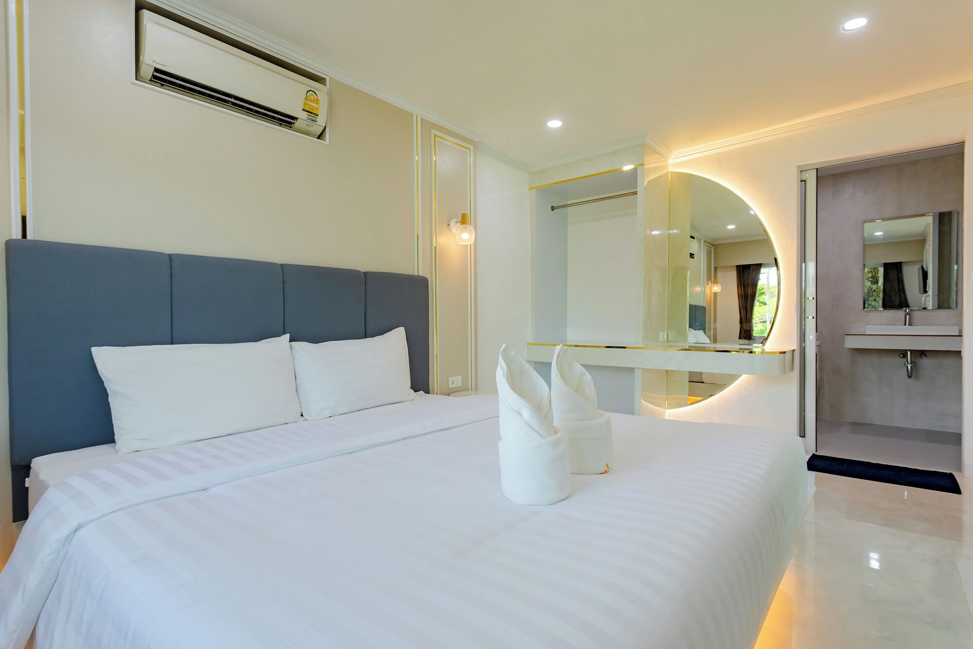 A modern hotel room with a large bed, a bathroom with a mirror, and an air conditioning unit.