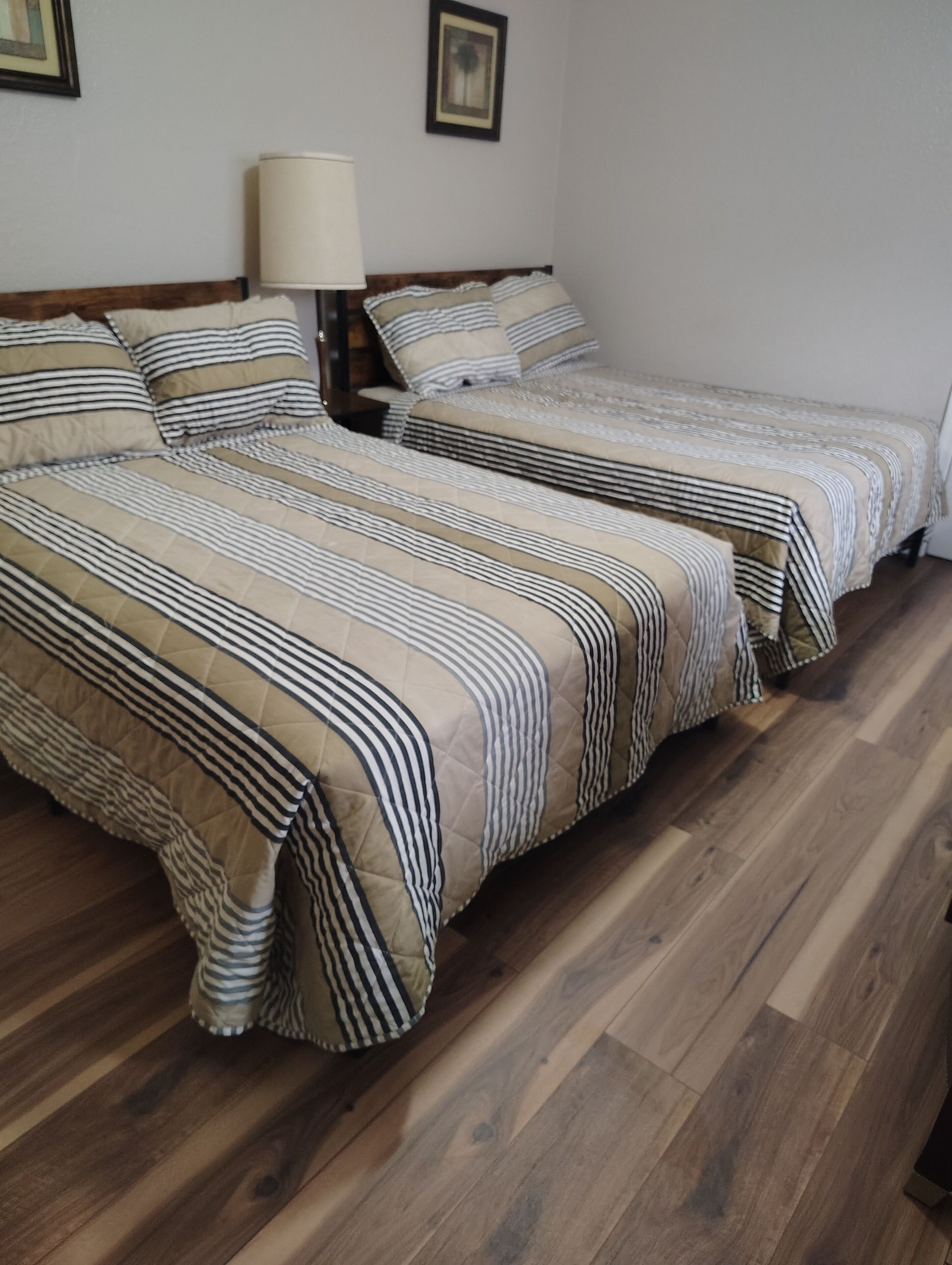 Una habitación con dos camas, suelo de madera y una lámpara en la mesita de noche.