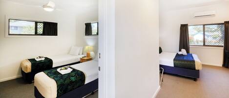 A hotel room with two beds, a desk, a chair, a lamp, and an air conditioning unit.