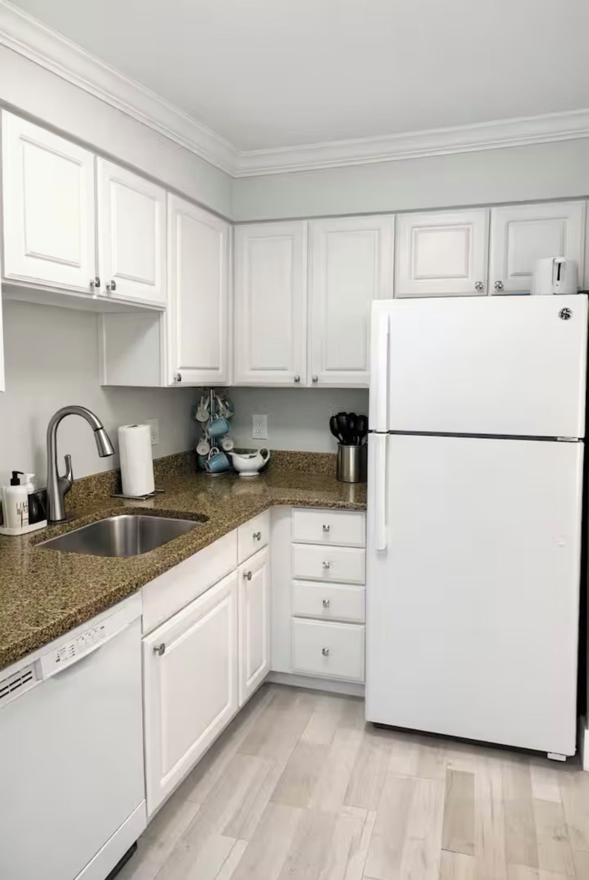 A kitchen with white cabinets, a stainless steel sink, and a white refrigerator.