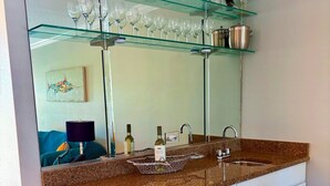 A kitchen with a granite countertop, white cabinetry, a glass shelf above the sink holding wine glasses, and a decorative bird sculpture.