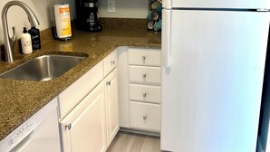 A kitchen with white cabinets, a stainless steel sink, a coffee maker, and a refrigerator.