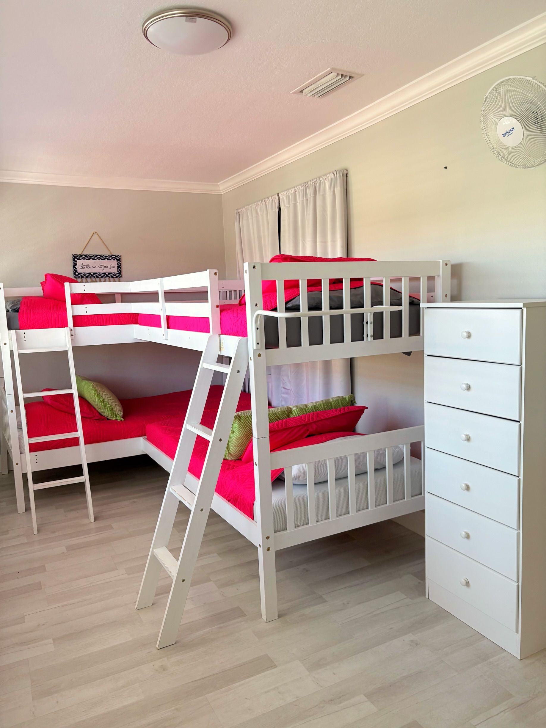 Een slaapkamer met stapelbed, een witte dressoir en een ladder.