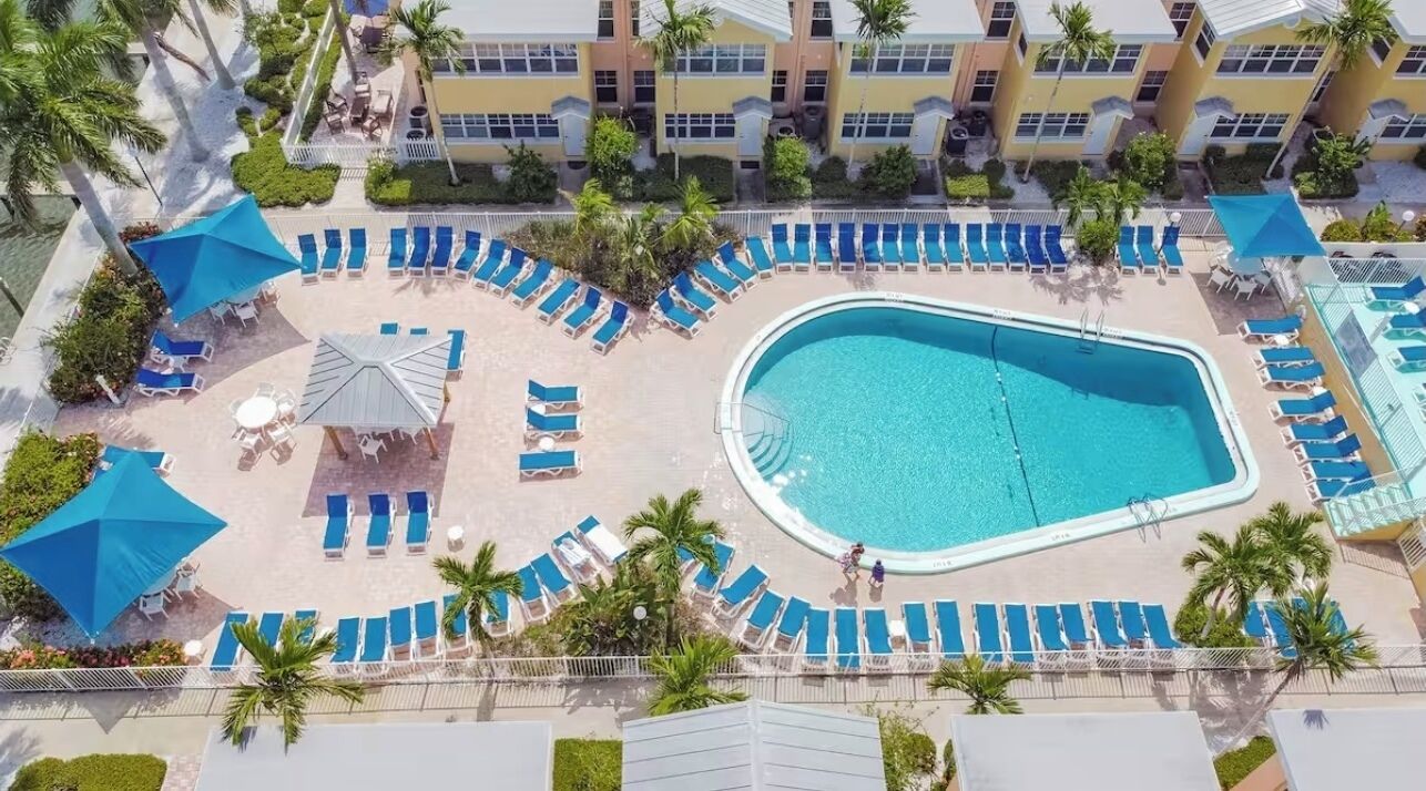 Luchtbeeld van een resort met een groot zwembad, ligbedden en palmbomen.