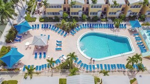 An aerial view of a resort with a large pool, sun loungers, and palm trees.