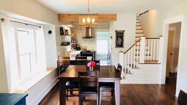 A spacious kitchen with wooden flooring, a dining area with a wooden table and chairs, and a staircase leading to an upper level. - The Perry Canary: Newly Renovated, Charming, Walk to Coffee and Restaurants (Spokane)