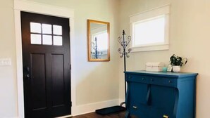 A room with a dark wooden door, a blue dresser, a mirror, and a window with blinds. - The Perry Canary: Newly Renovated, Charming, Walk to Coffee and Restaurants (Spokane)