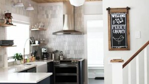 A modern kitchen with a central island, wooden ceiling beams, and a chalkboard sign on the wall. - The Perry Canary: Newly Renovated, Charming, Walk to Coffee and Restaurants (Spokane)