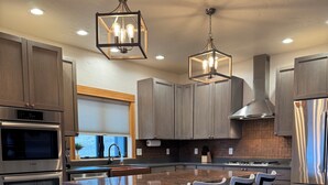 Una cocina moderna con una isla central, taburetes de bar, electrodomésticos de acero inoxidable e iluminación colgante.
