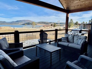 A covered deck with outdoor furniture, a grill, and a view of a lake and mountains. - Lakeview Lodge- ADA Accessible Retreat Close To The Water (Anaconda)