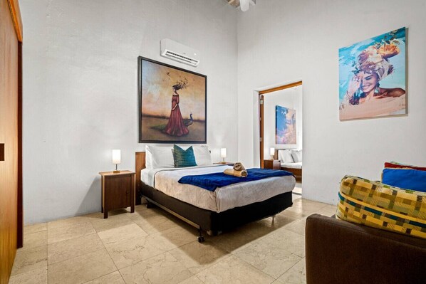 Un dormitorio con cama, mesitas de noche, una silla y obras de arte en las paredes.