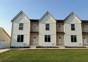 A row of three-story townhouses with a uniform architectural style, featuring a central entrance and a small front yard with landscaping. - Beautiful European Style Townhome - Near ISU (Pocatello)
