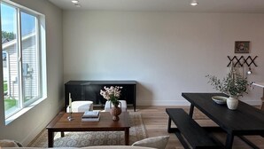 Un salon moderne avec une grande fenêtre, une table en bois foncé, un canapé et un meuble de rangement noir pour les appareils multimédias.
