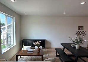 A modern living room with a large window, a dark wooden table, a sofa, and a black entertainment unit. - Beautiful European Style Townhome - Near ISU (Pocatello)