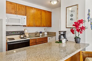 A kitchen with wooden cabinets, a microwave, a stove, a coffee maker, and a framed picture on the wall.