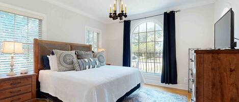 A bedroom with a large bed, a chandelier, a TV, and a view of the outdoors.