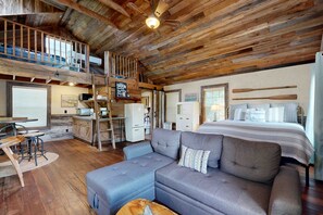A rustic cabin interior with a loft bedroom, a dining area, and a kitchen.