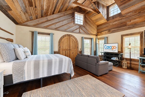 A spacious room with a large bed, a sofa, a television, and a wooden ceiling.