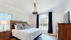 A bedroom with a large bed, a chandelier, a TV, and a view of the outdoors. - Charming Spanish-Style Home in the Heart of Davis Shores (St. Augustine)