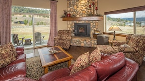 A cozy living room with a stone fireplace, leather sofa, and a large window offering a scenic view.