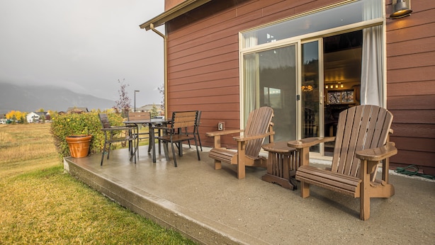 A wooden deck with outdoor furniture, including chairs and a table, in front of a house with a large glass door.