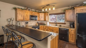 A kitchen with wooden cabinets, a black refrigerator, a dishwasher, and a bar area with stools.