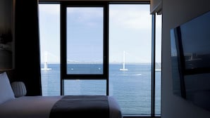 Habitación de hotel con un ventanal que ofrece vistas a un puente y al mar.
