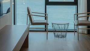 Habitación moderna con un ventanal grande que da a un puente y al agua. Hay dos sillas y una mesita.