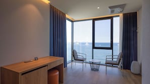 Una habitación moderna con un escritorio de madera, dos sillas, una mesita redonda y vistas al mar y a un puente.