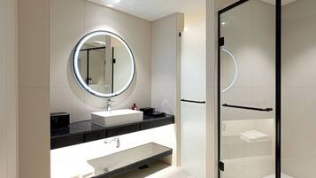 A modern bathroom with a round mirror, a white sink, a black countertop, and a glass-enclosed shower area.