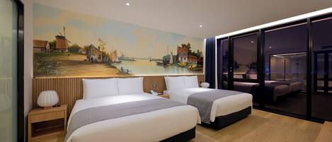 Una habitación de hotel moderna con dos camas, un cuadro grande de una escena costera en la pared y vistas a la ciudad a través de amplios ventanales.