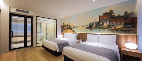 A hotel room with two beds, a painting of a village scene on the wall, a wooden floor, and a desk with a lamp.
